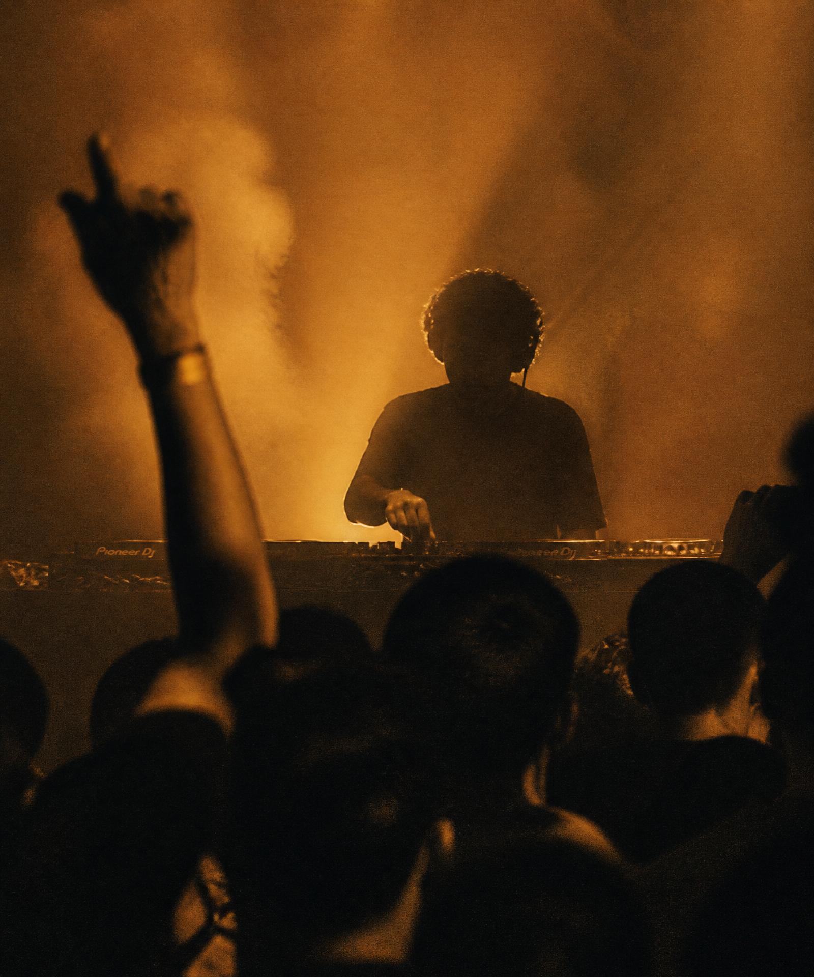 DJ silhouette behind decks with amber haze